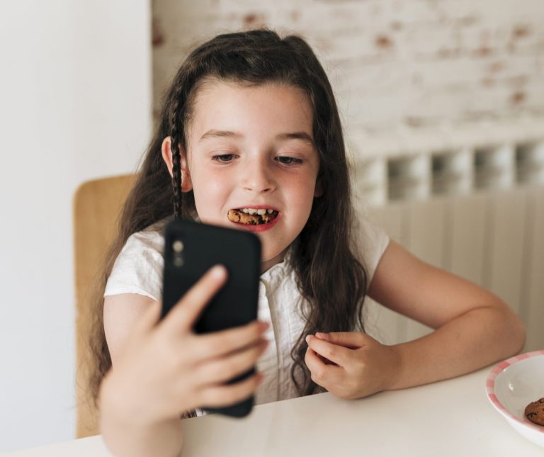 garota-de-alto-angulo-com-telefone-comendo-biscoitos