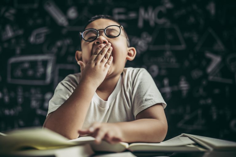 A boy with glasses studying and drowsy